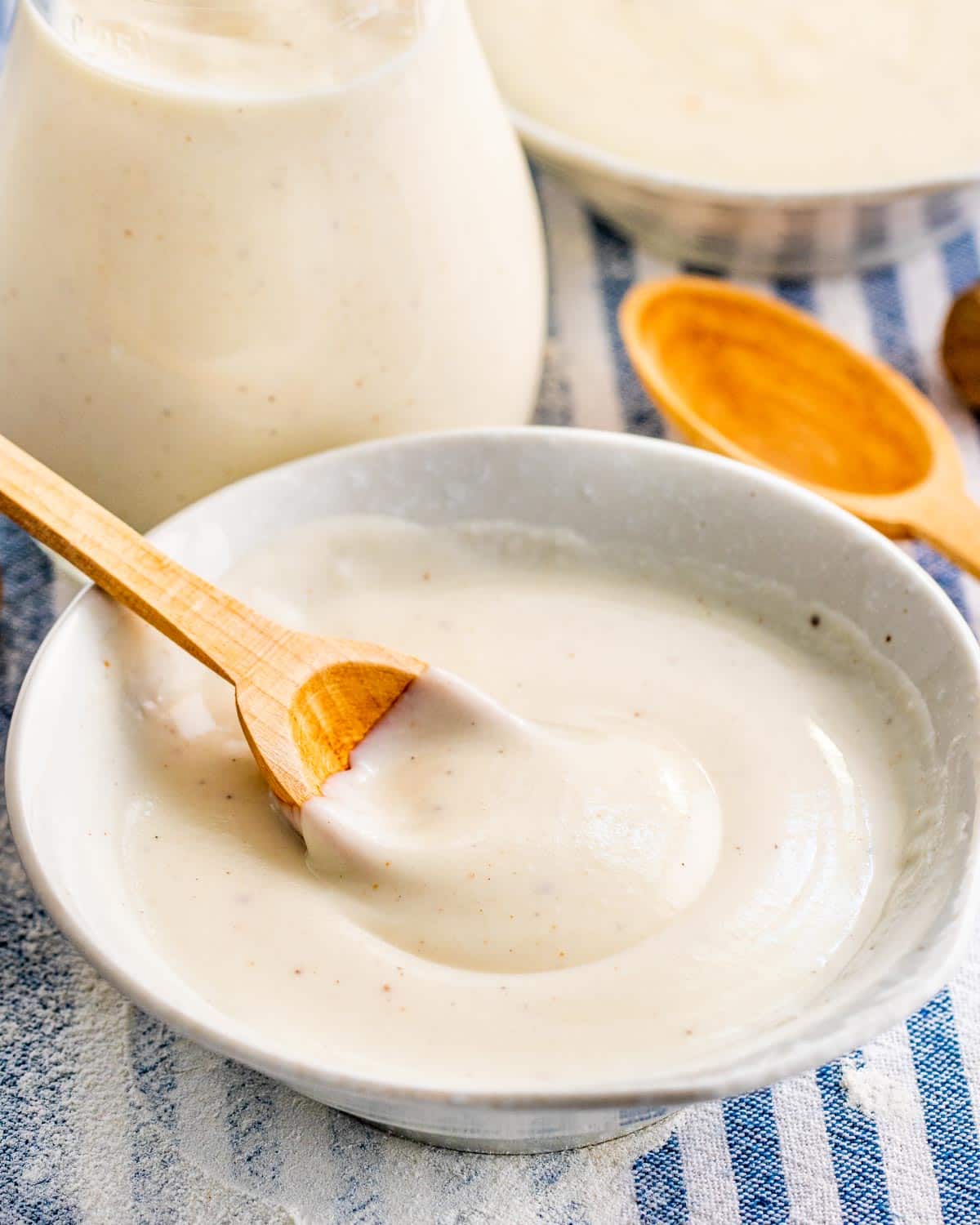 bechamel sauce in a small white bowl with a mini wooden spoon inside