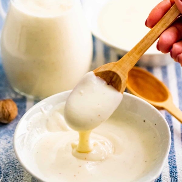 bechamel sauce in a white bowl with a hand taking a spoonful of it