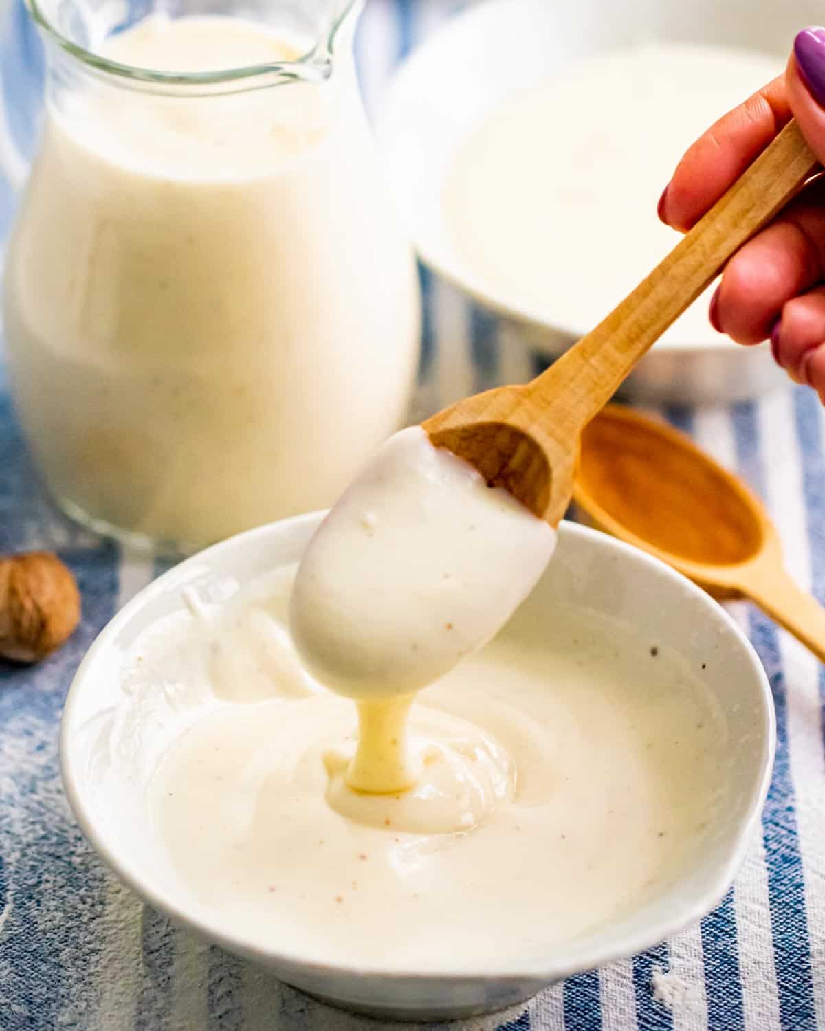bechamel sauce in a white bowl with a hand taking a spoonful of it