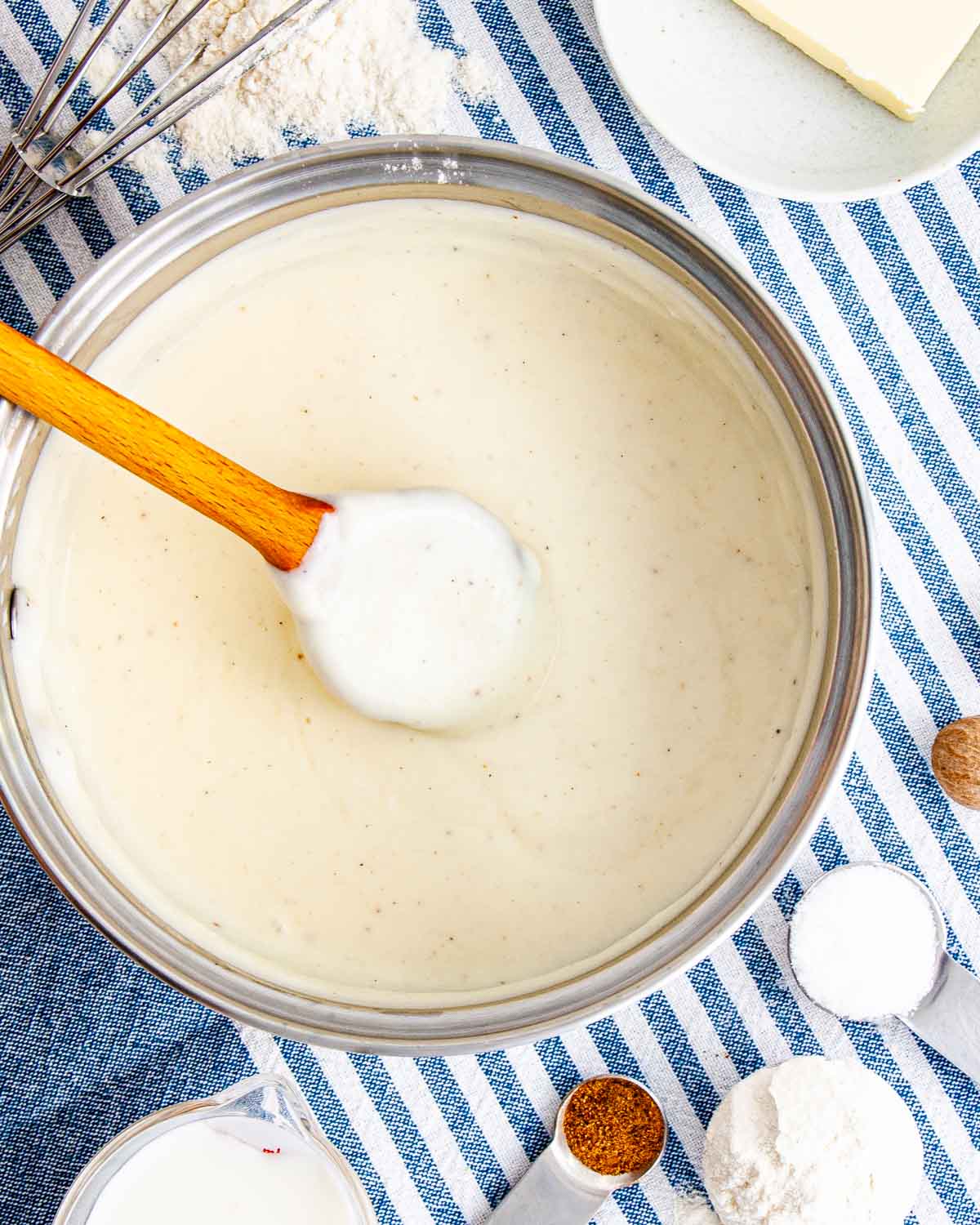 overhead shot of freshly made bechamel sauce in a saucepan with a wooden spoon inside