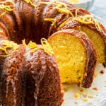 side view shot of a lemon orange bundt cake drizzled with honey lemon icing and garnished with lemon zest. Two slices are cut from the cake