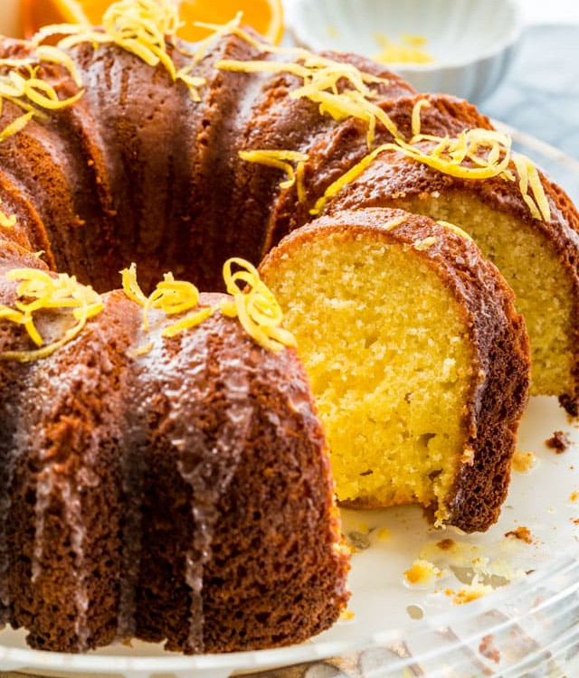 side view shot of a lemon orange bundt cake drizzled with honey lemon icing and garnished with lemon zest. Two slices are cut from the cake