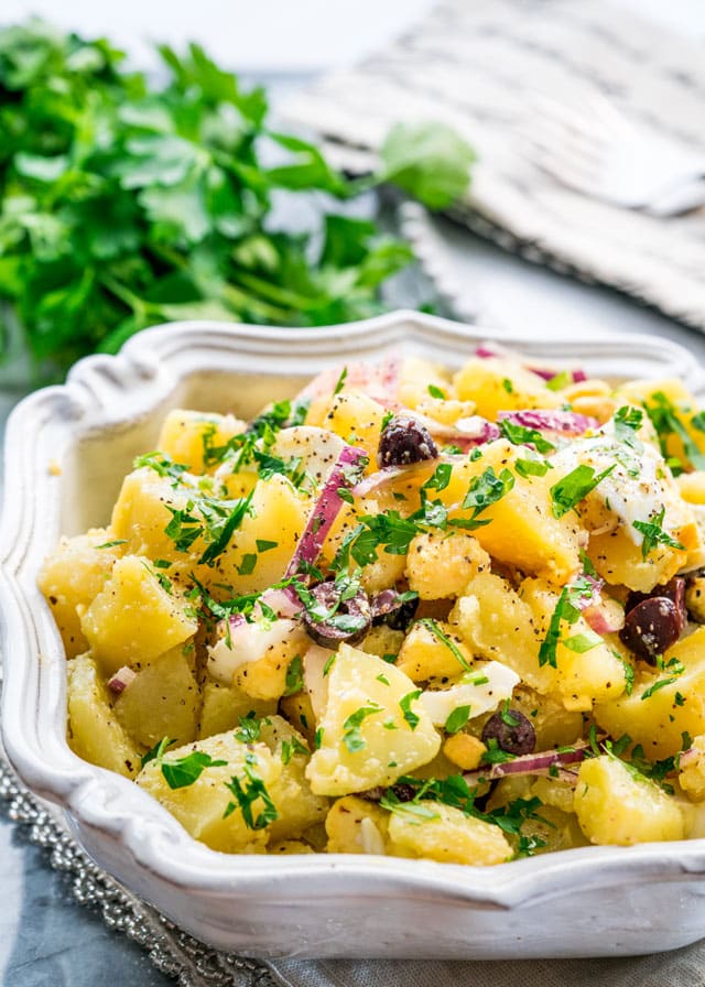 a large bowl of potato salad with eggs, onions, parsley, and olives