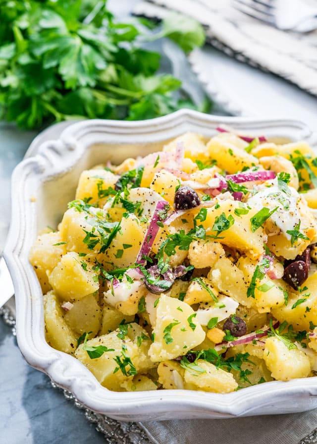 a large bowl full of potato salad with onions, olives, and parsley