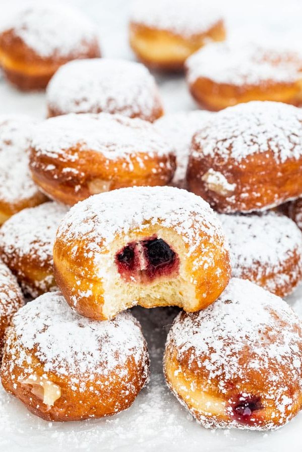 side view shot of paczki dusted with powdered sugar with a bite taken out of one