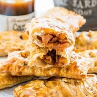 a stack of apple turnovers dripping with caramel sauce, one ripped in half exposing the center