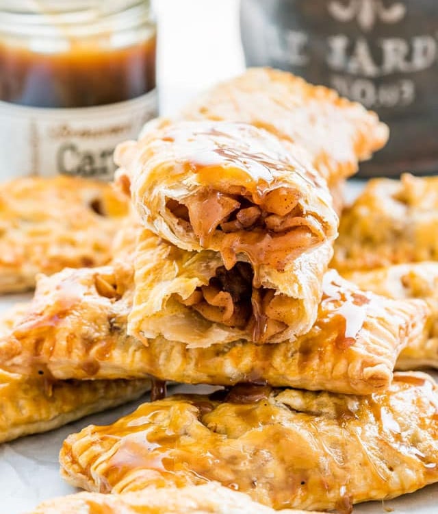 a stack of apple turnovers dripping with caramel sauce, one ripped in half exposing the center