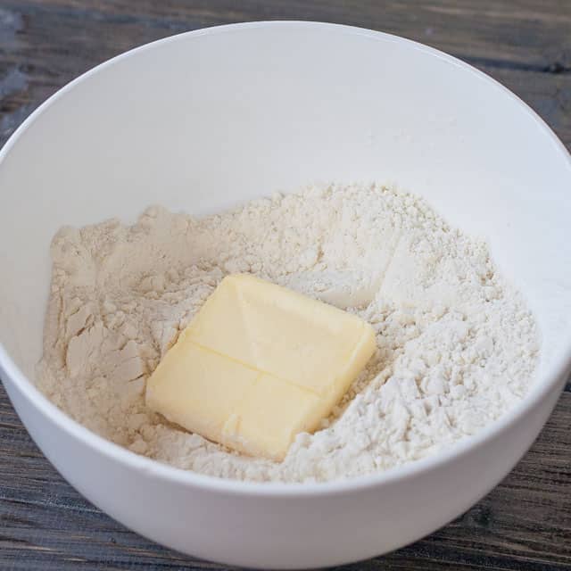 A bowl full of flour, baking powder and salt with a small piece of butter in the middle