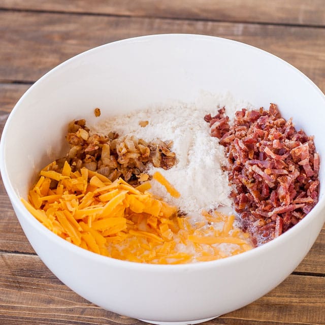 Bacon, fried onion and cheddar cheese are added to the bowl of flour.