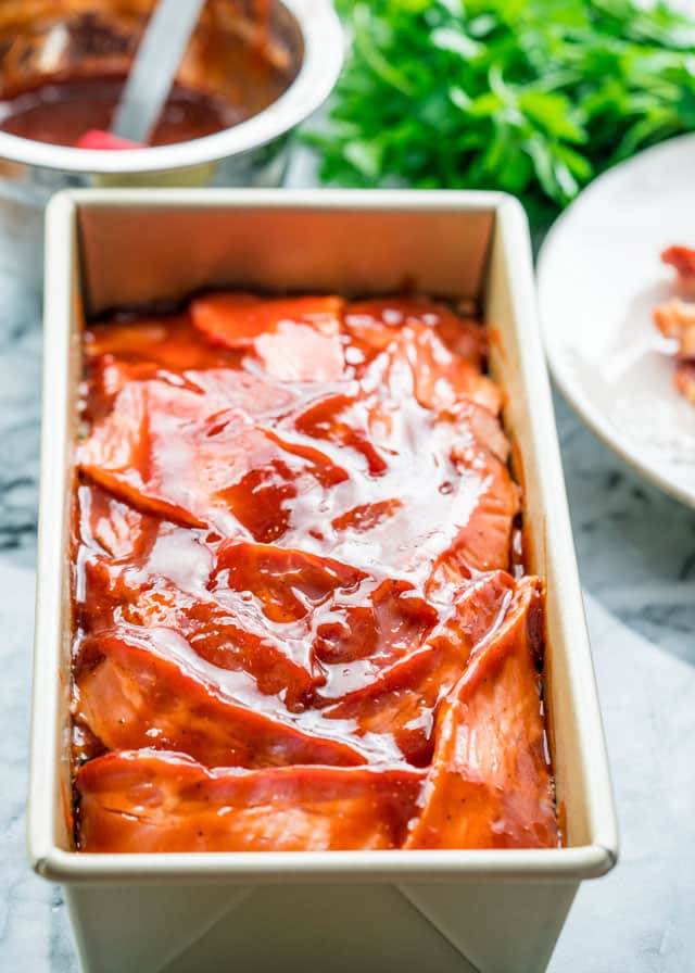 a loaf pan with meatloaf topped with bacon and bbq sauce