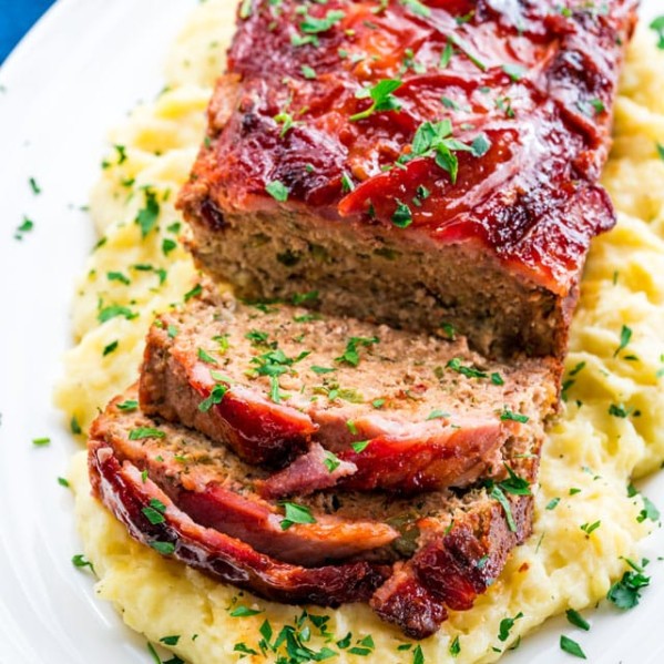top shot of a plate of mashed potatoes with the bacon wrapped meatloaf on top. Two slices have been cut