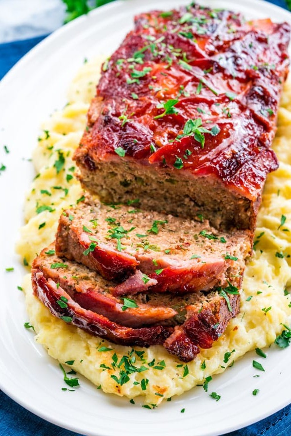 top shot of a plate of mashed potatoes with the bacon wrapped meatloaf on top. Two slices have been cut