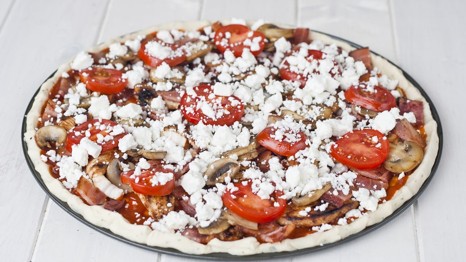 Tomatoes and more feta are added to the pizza.