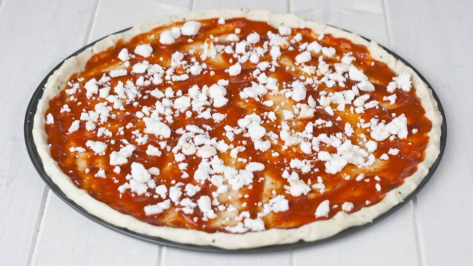 Feta cheese layered over top the tomato sauce on the uncooked pizza dough.