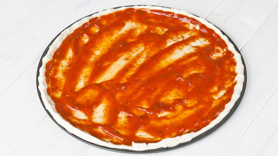 Uncooked pizza crust topped with tomato sauce