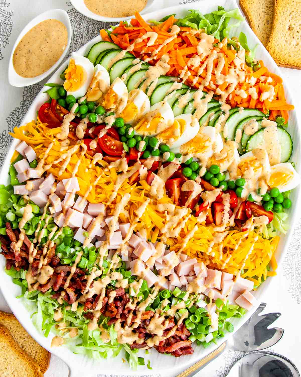 overhead shot of a layered chef salad drizzled with a homemade dressing in a white serving bowl