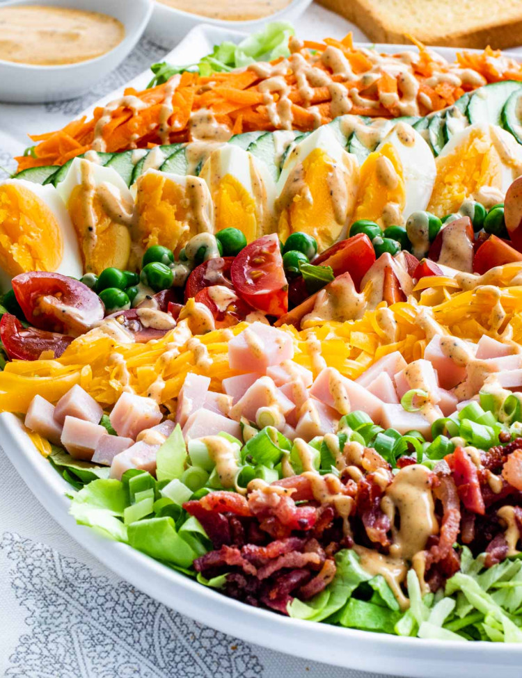 sideview shot of a layered chef salad drizzled with a homemade dressing in a white serving bowl