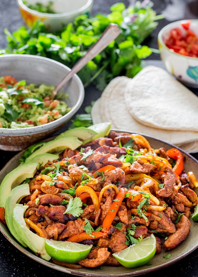 Pork Fajitas on a plate with lime wedges and slices of avocado