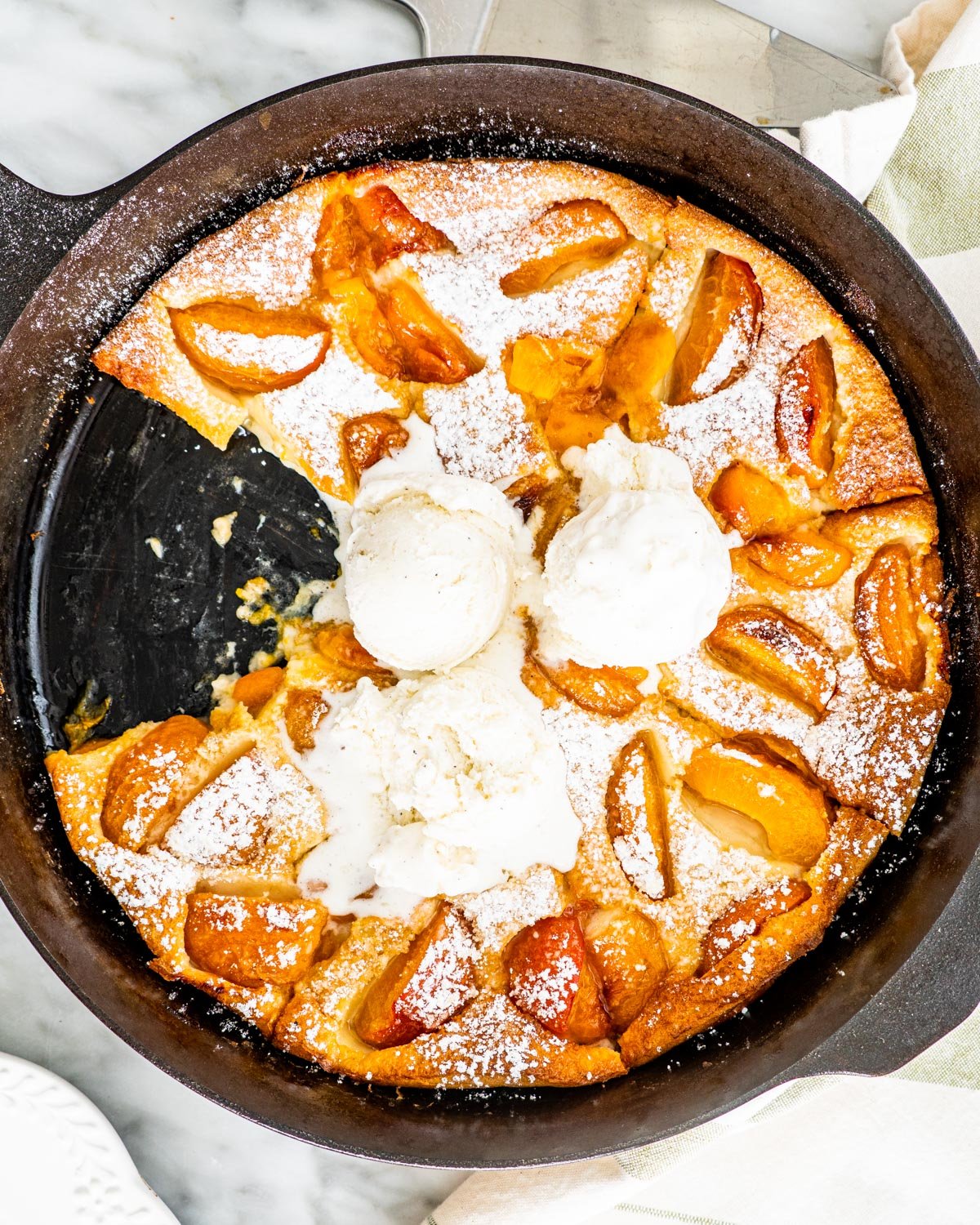 overhead shot of apricot clafoutis in a black skillet with a couple scoops of ice cream on it