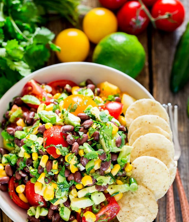 overhead shot of a bowl of black bean corn avocado salad garnished with tortilla chips