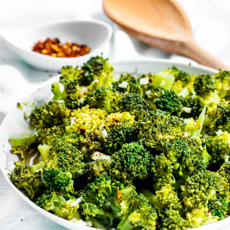 side view shot of broccoli salad in a white bowl with a wooden spoon in the background