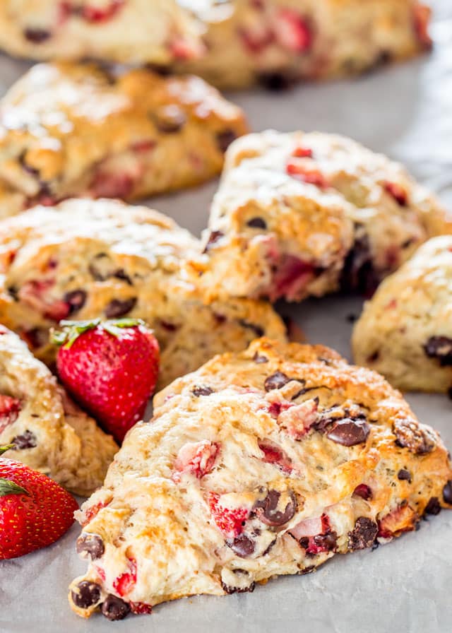 strawberry chocolate chip scones on parchment paper with 2 fresh strawberries