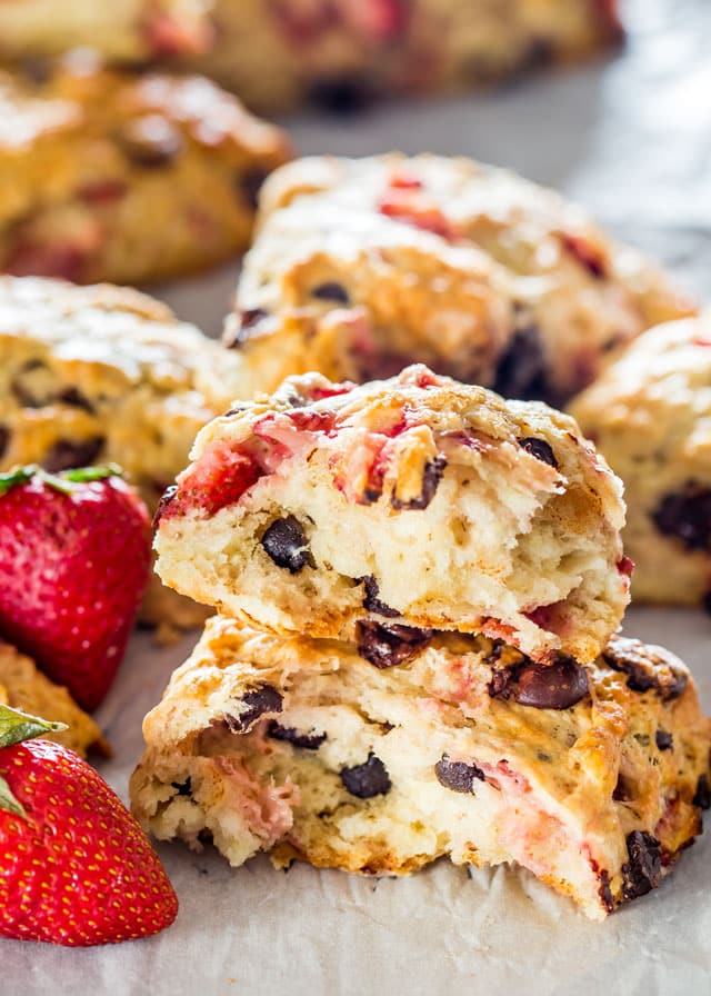 strawberry chocolate chip scones split in half and stacked on each other with 2 fresh strawberries
