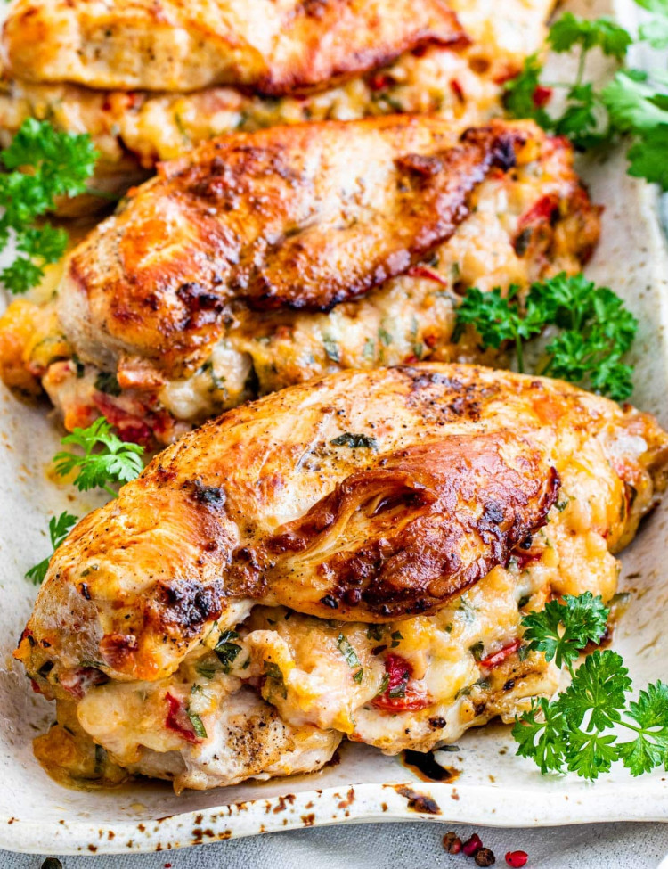 side view shot of 3 stuffed chicken breasts with roasted peppers and asiago cheese on a serving platter and garnished with parsley