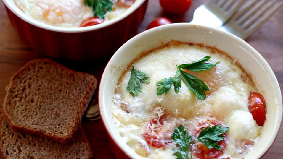 Top shot of finished Baked Eggs with Leeks, Tomatoes and Prosciutto, garnished with parsley and served with a slice of bread
