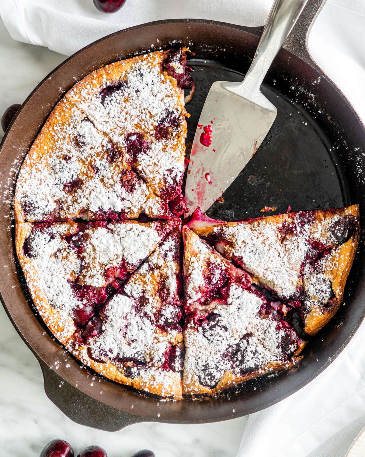 overhead shot of a cherry clafoutis cut into slices and dusted with powdered sugar