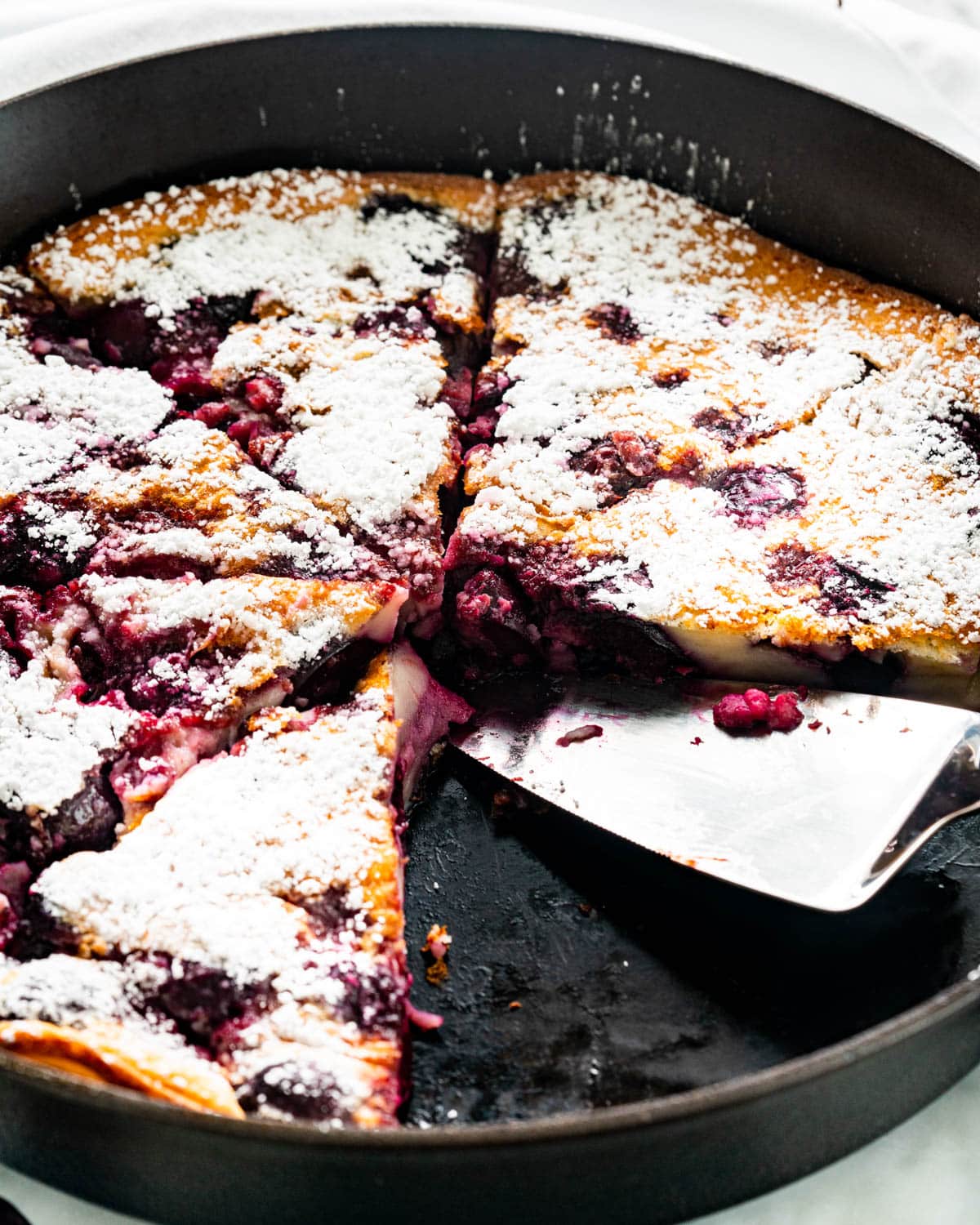 cherry clafoutis in a skillet with 2 slices taken out of it and dusted with powdered sugar