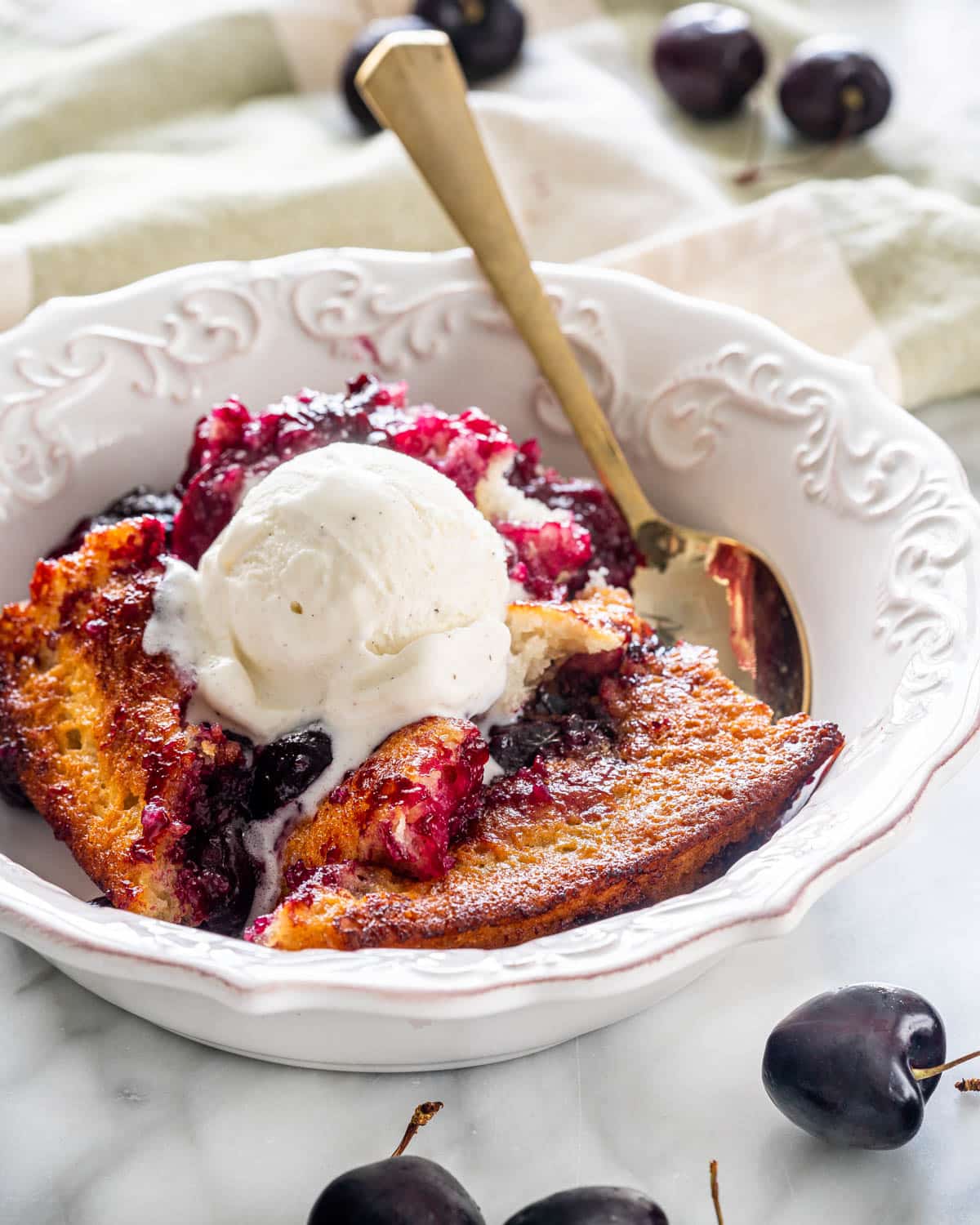 cherry cobbler in a white bowl with a scoop of ice cream