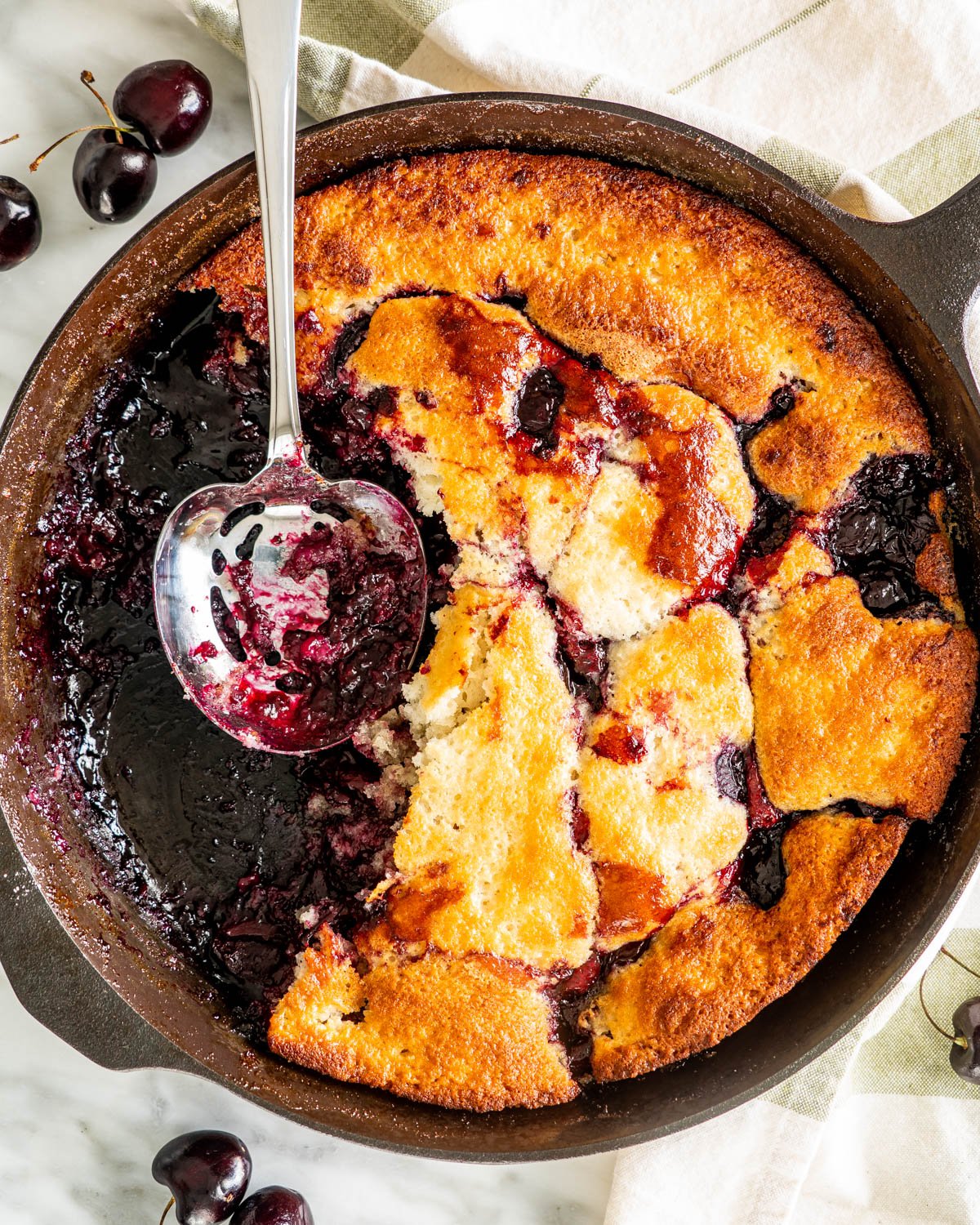 overhead shot of cherry cobbler in a black skillet with a spoon 