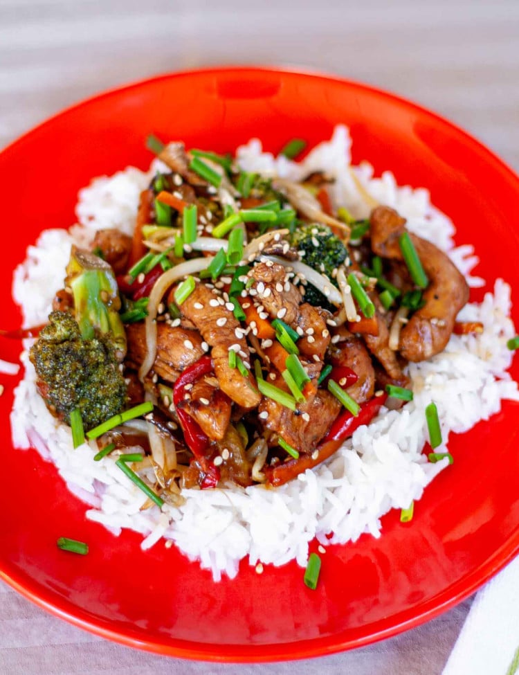 chicken stir fry on a bed of rice on a red plate.