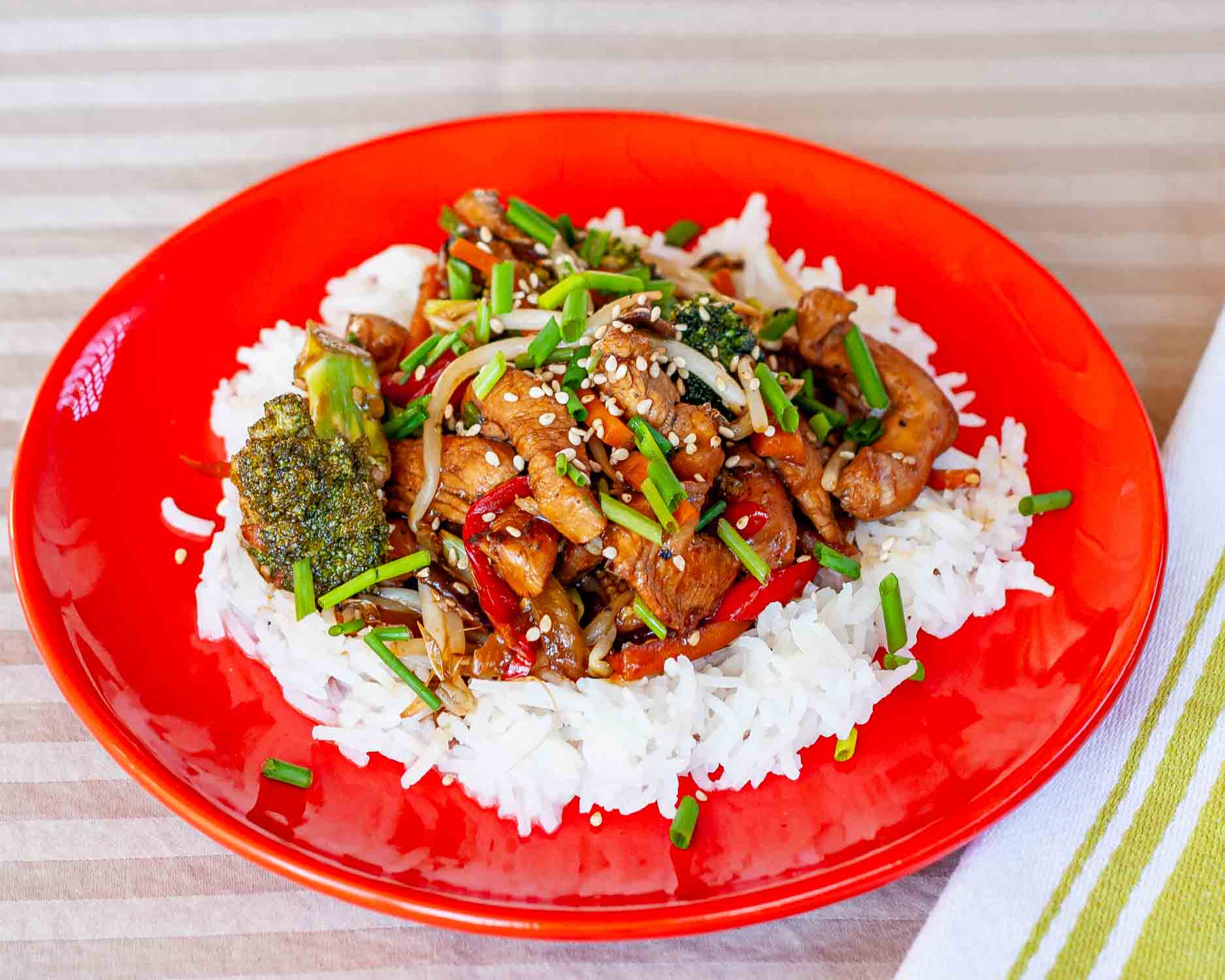 chicken stir fry on a bed of rice on a red plate.