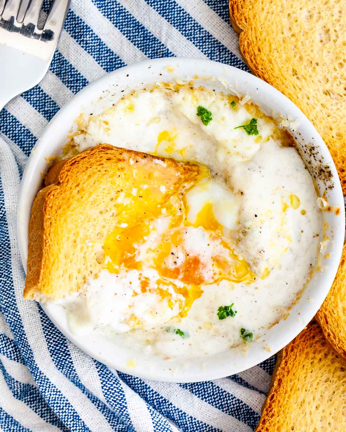overhead shot of creamy baked eggs with a piece of toast dunked in it