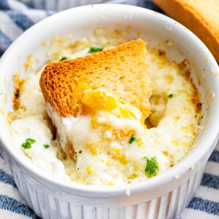 a piece of toast dunked in a ramekin with creamy baked eggs
