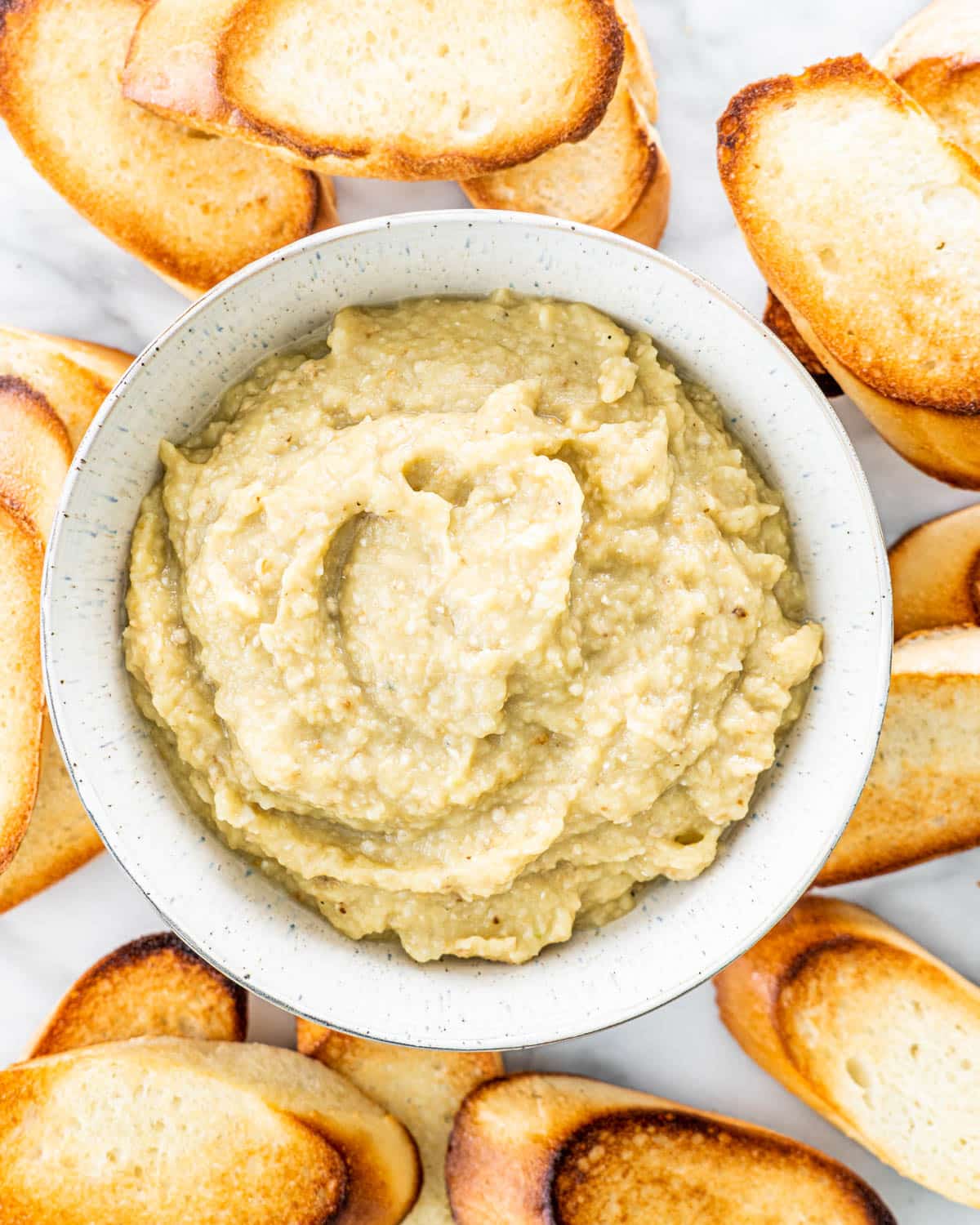 overhead shot of eggplant dip in a bowl surrounded by toasted bread