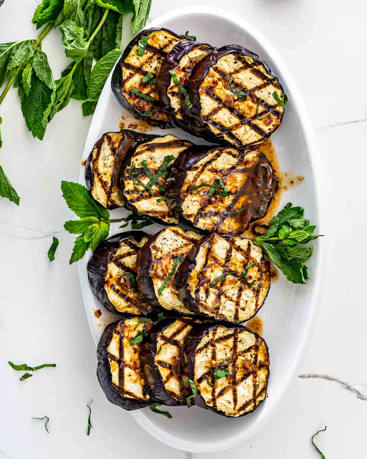 grilled eggplant with garlic mint sauce on a white platter.