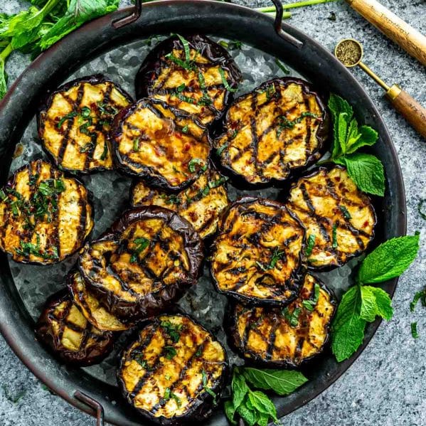 grilled eggplant with garlic mint sauce on a metal platter.