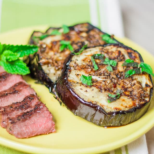 grilled eggplant with garlic sauce and mint on a plate next to a sliced steak