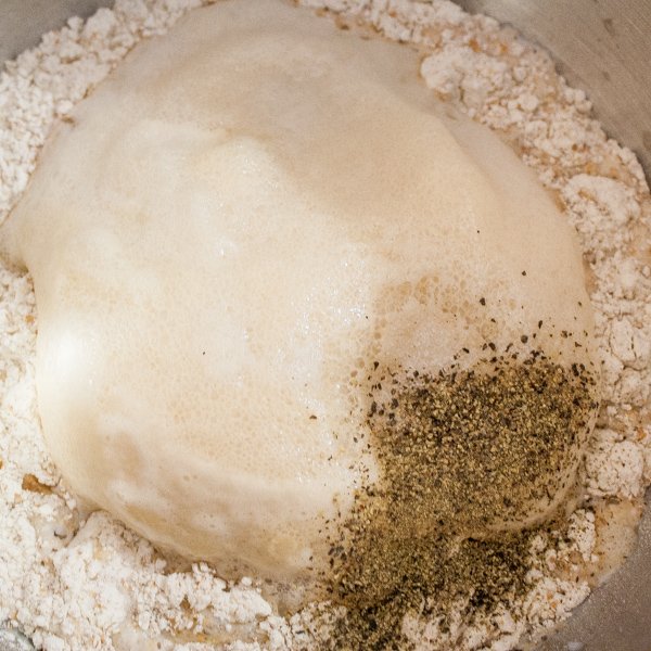 A bowl of white flour, whole wheat flour, salt and pepper, milk, olive oil and foamy yeast mixture.