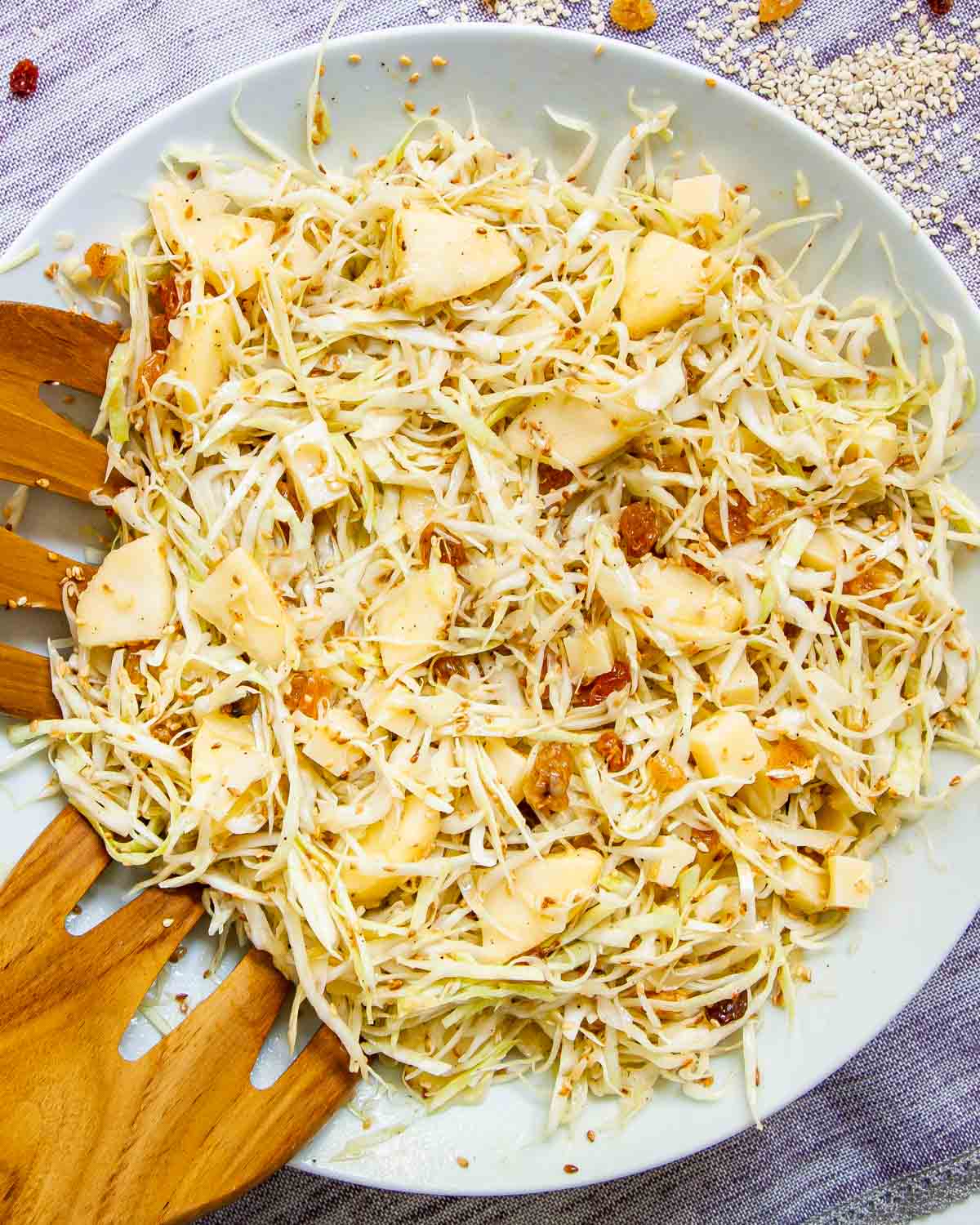 sesame cabbage salad in a large shallow white plate with 2 salad hands in it