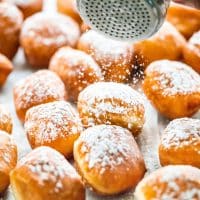 side view shot of a hand sprinkling powdered sugar over the beignets
