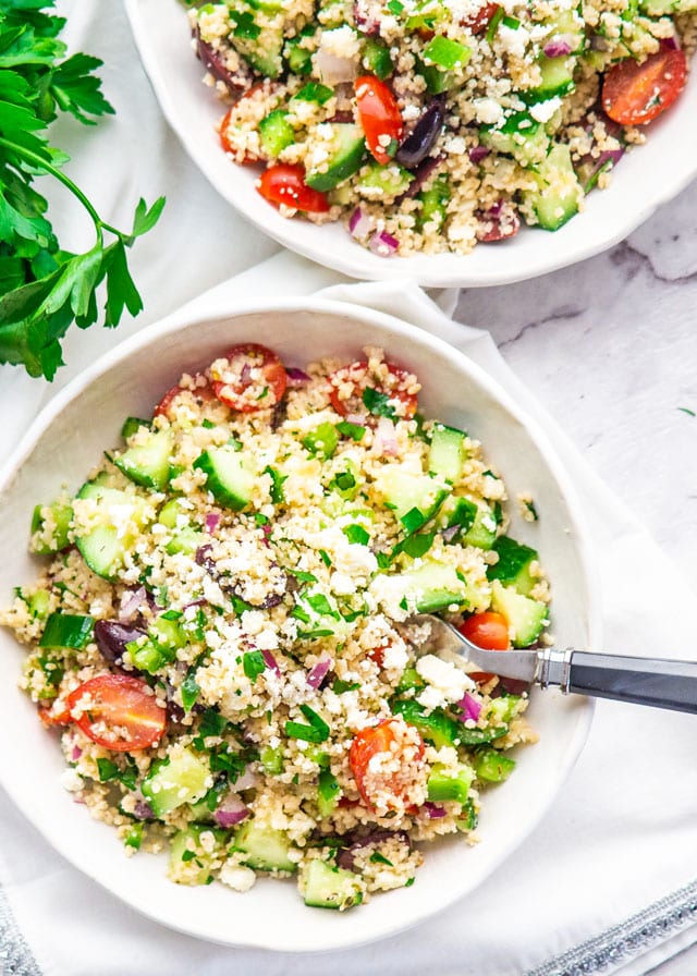 overhead shot of Mediterranean Couscous Salad in two white bowls with a fork in the bowl