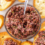 overhead shot of a bowl of olive tapenade surrounded by toasted baguette slices