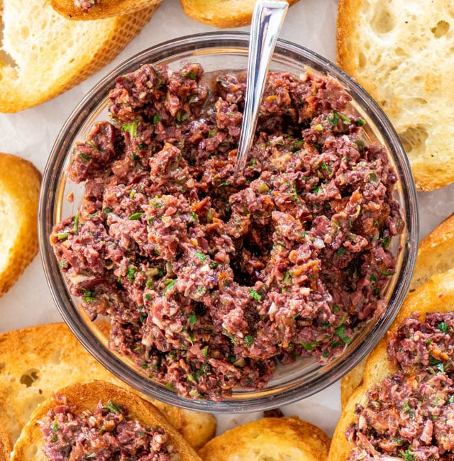 overhead shot of a bowl of olive tapenade surrounded by toasted baguette slices