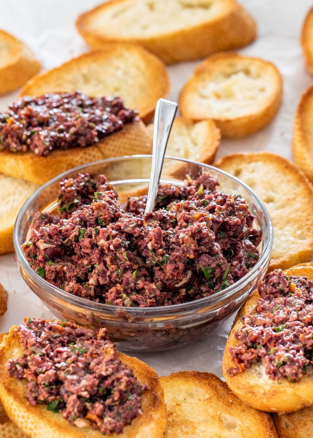 olive tapenade in a small bowl surrounded by crostini