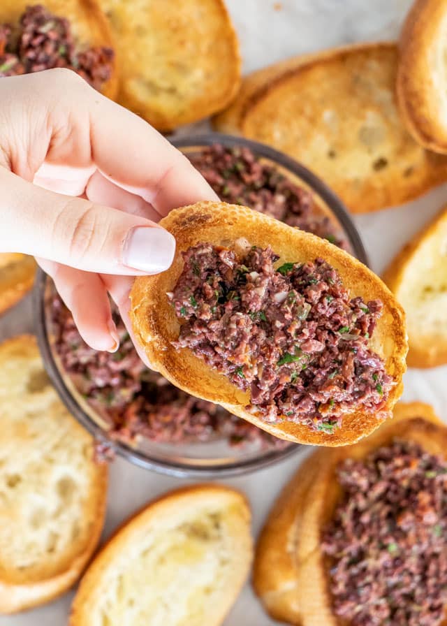 a hand holding an olive tapenade crostini
