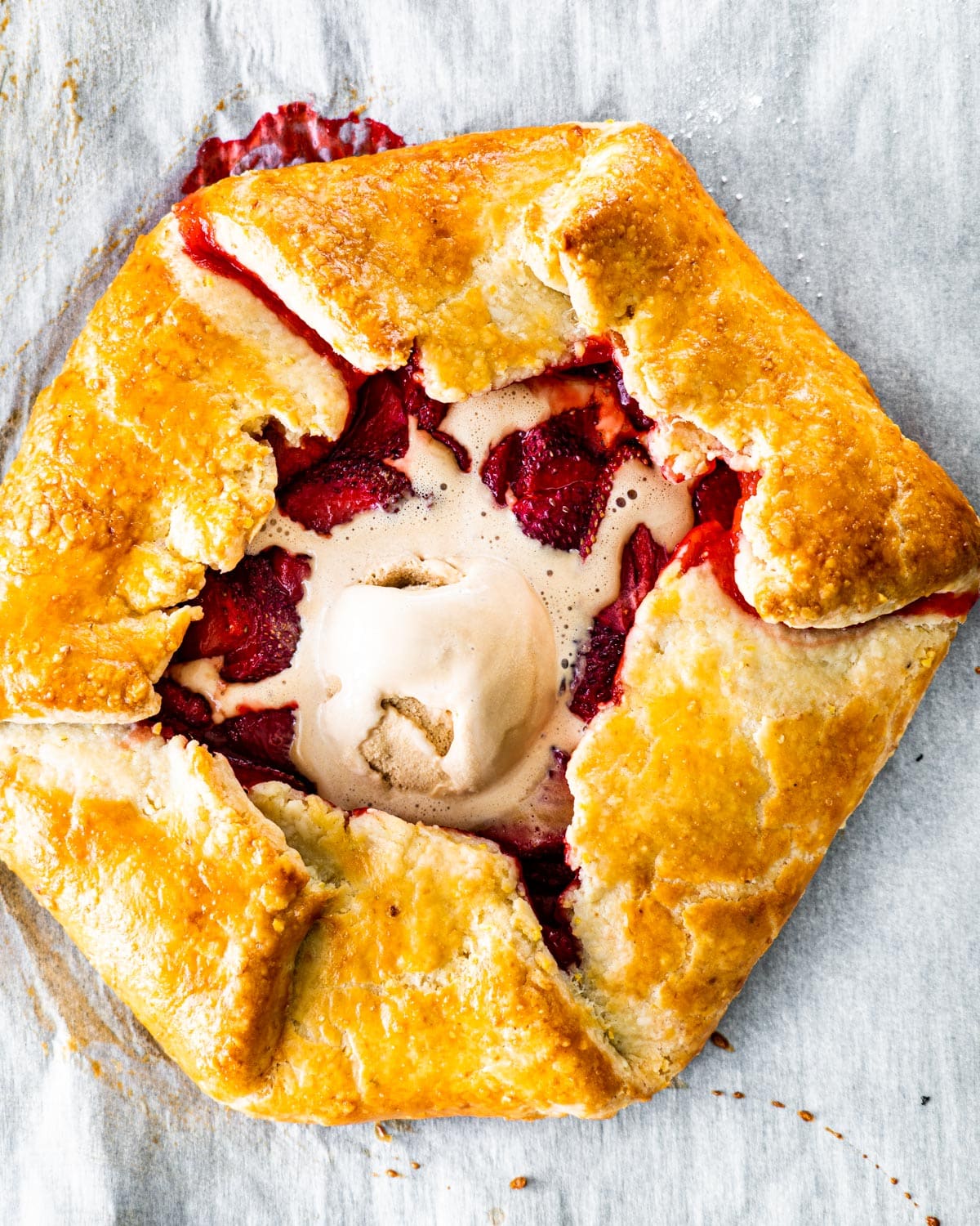 overhead shot of a strawberry galette with a scoop of ice cream on parchment paper